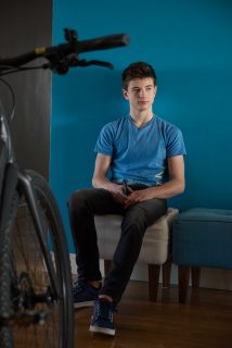 Boy in a blue t-shirt sits in front of a blue wall and bike in the foreground