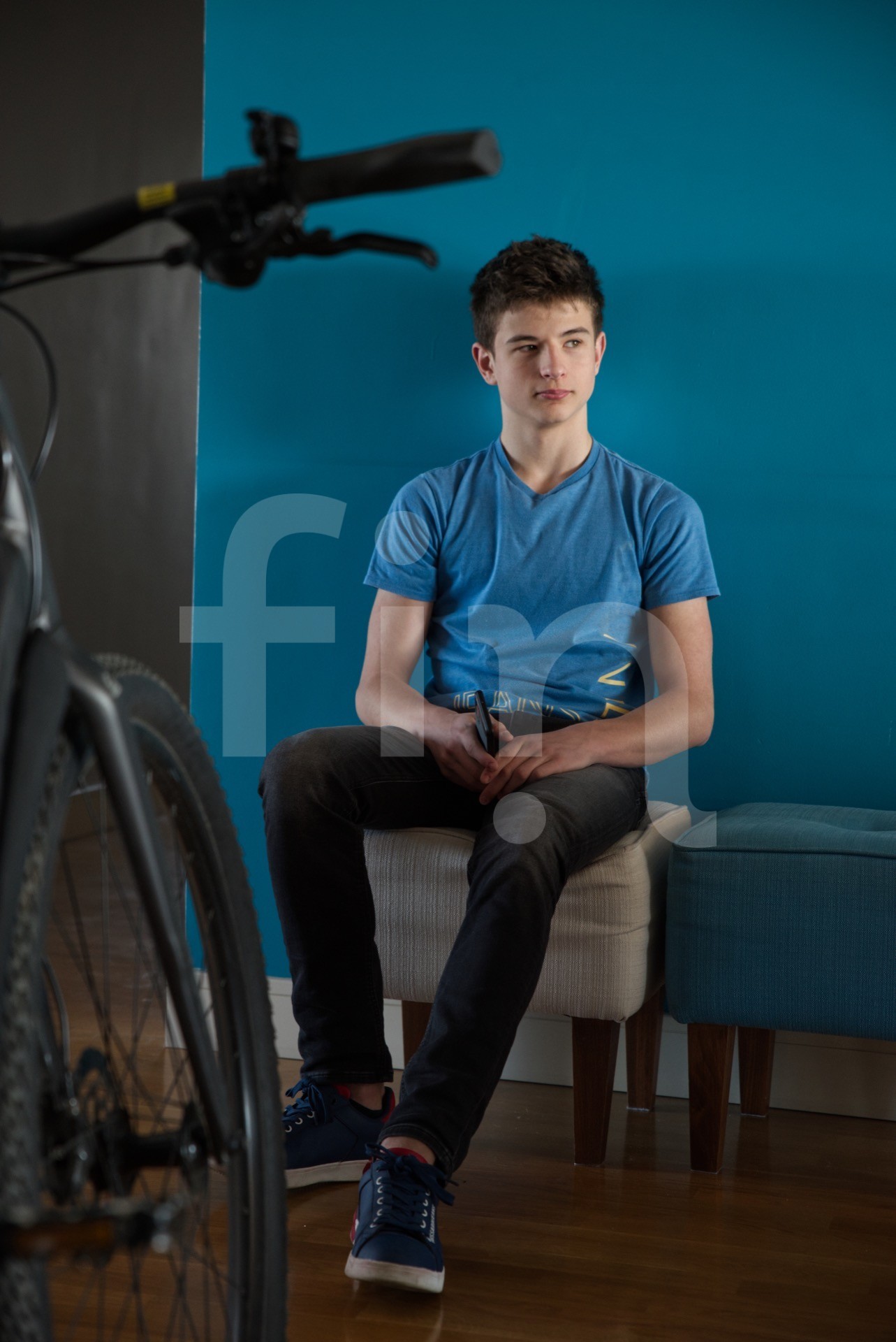 Boy in a blue t-shirt sits in front of a blue wall and bike in the foreground