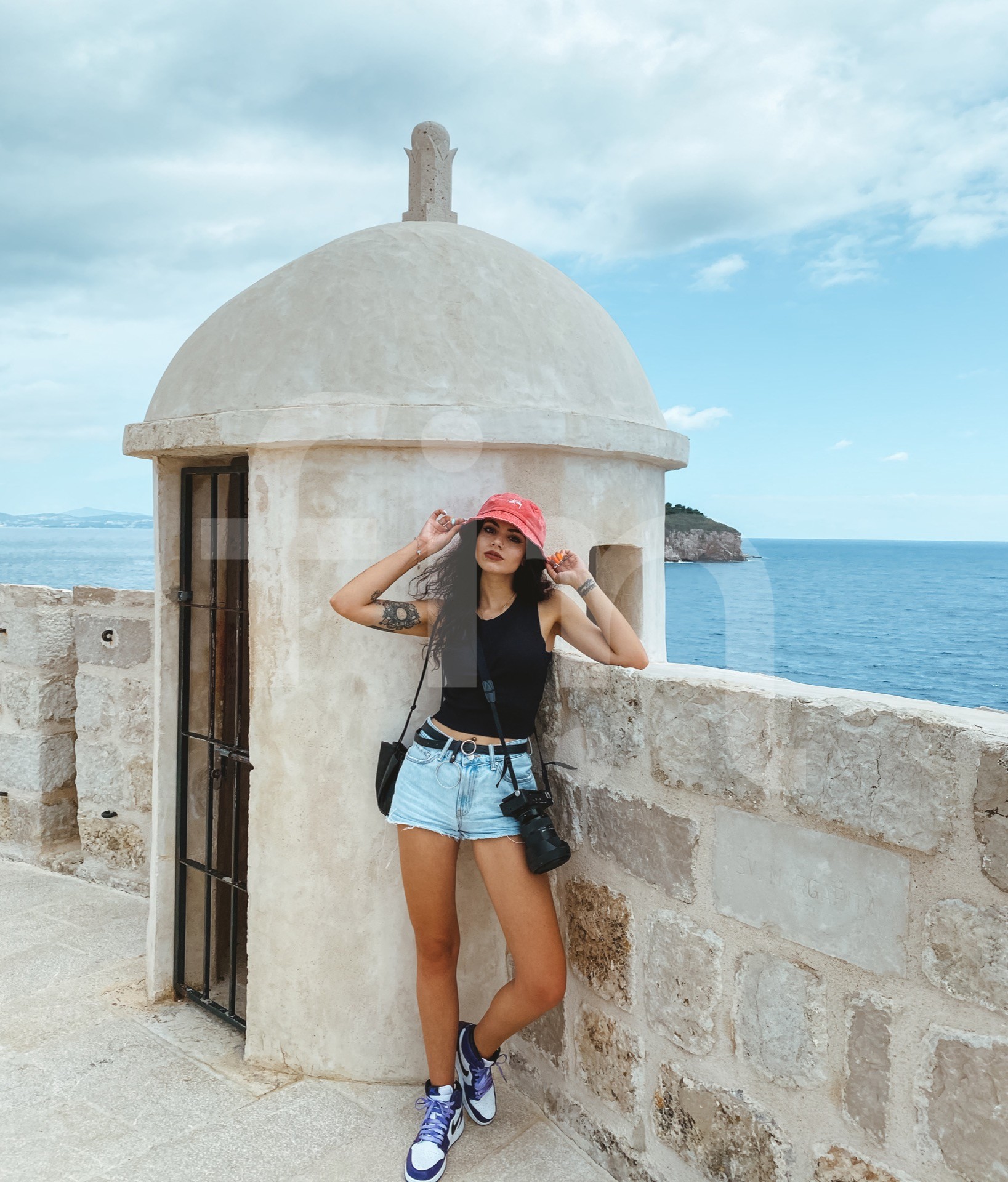Student girl with a red hat and a camera on the city walls in the background of the sea