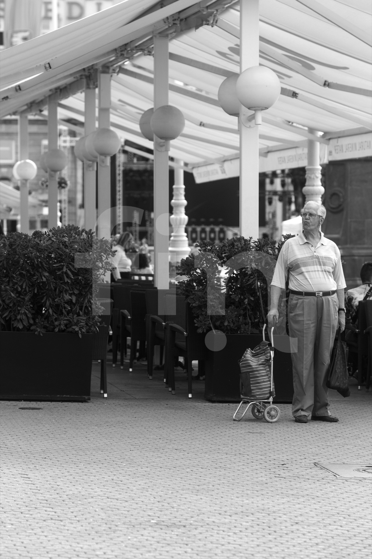 The older gentleman stands and waits with trolley dolley looking aside black and white