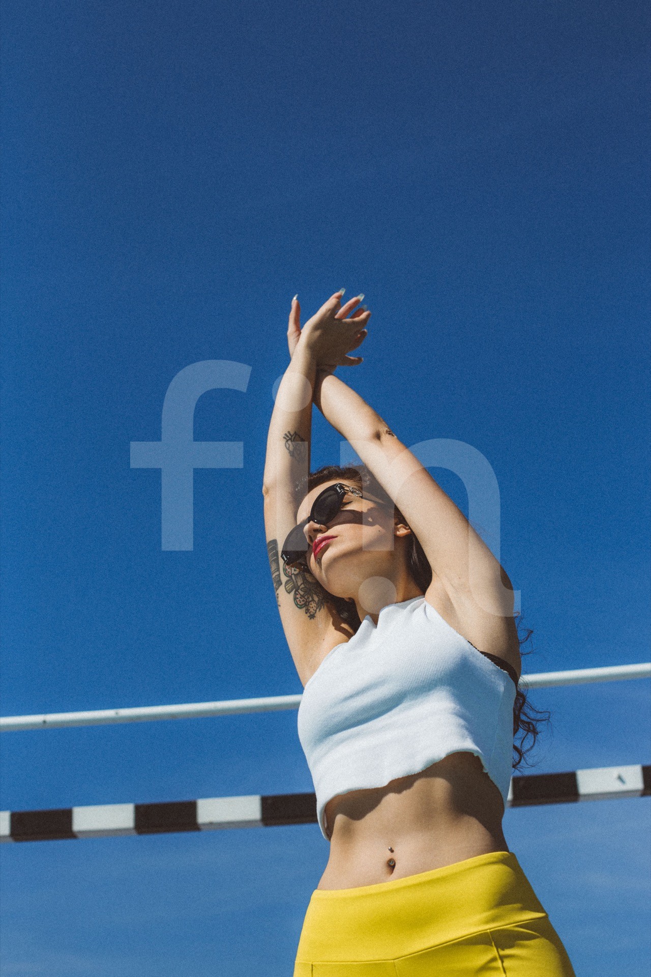 Girl with a sunglasses and hands raised in the air standing in front of a football tripod