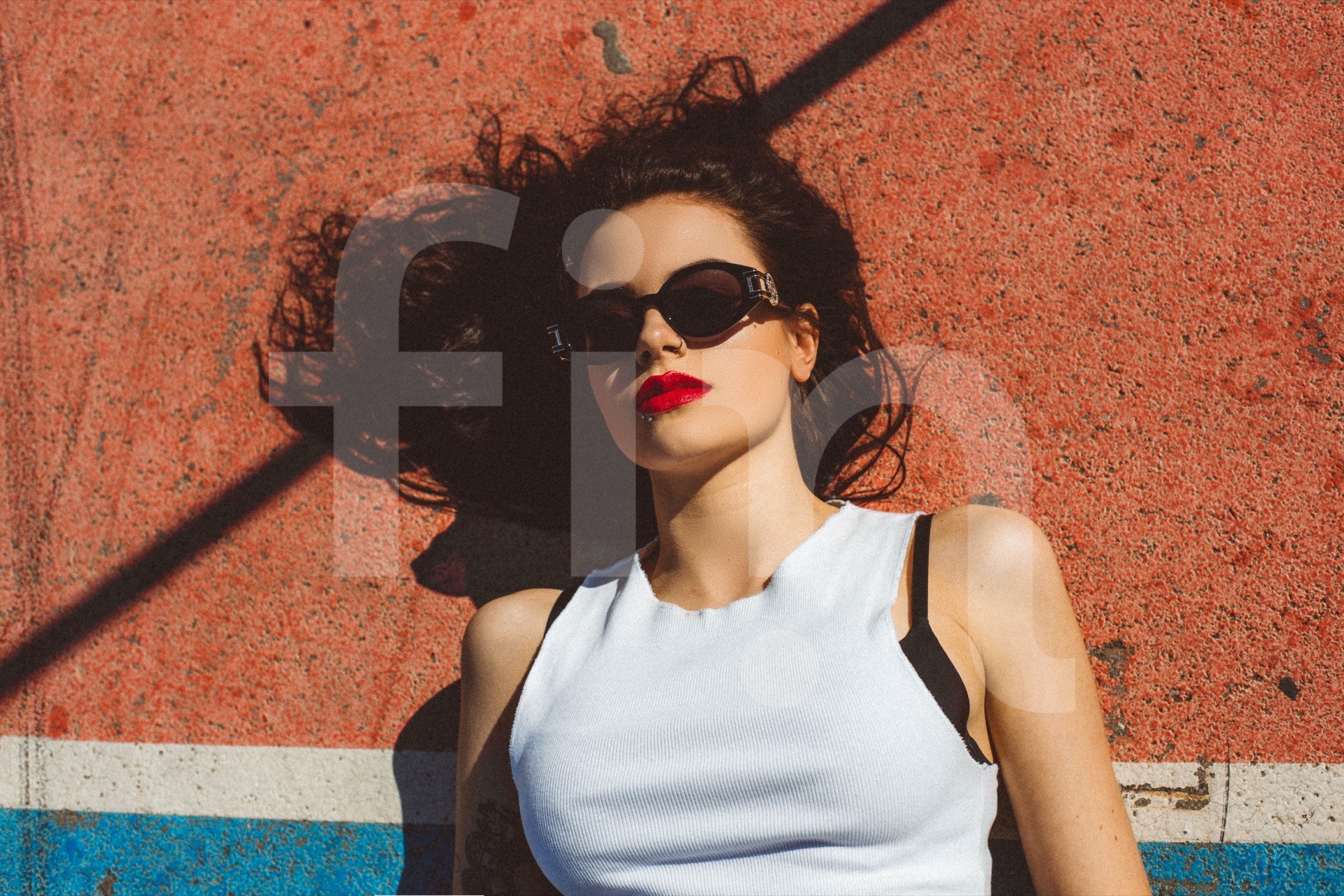 girl with a red lipstick an sunglasses lzing on sport field on a sunny day