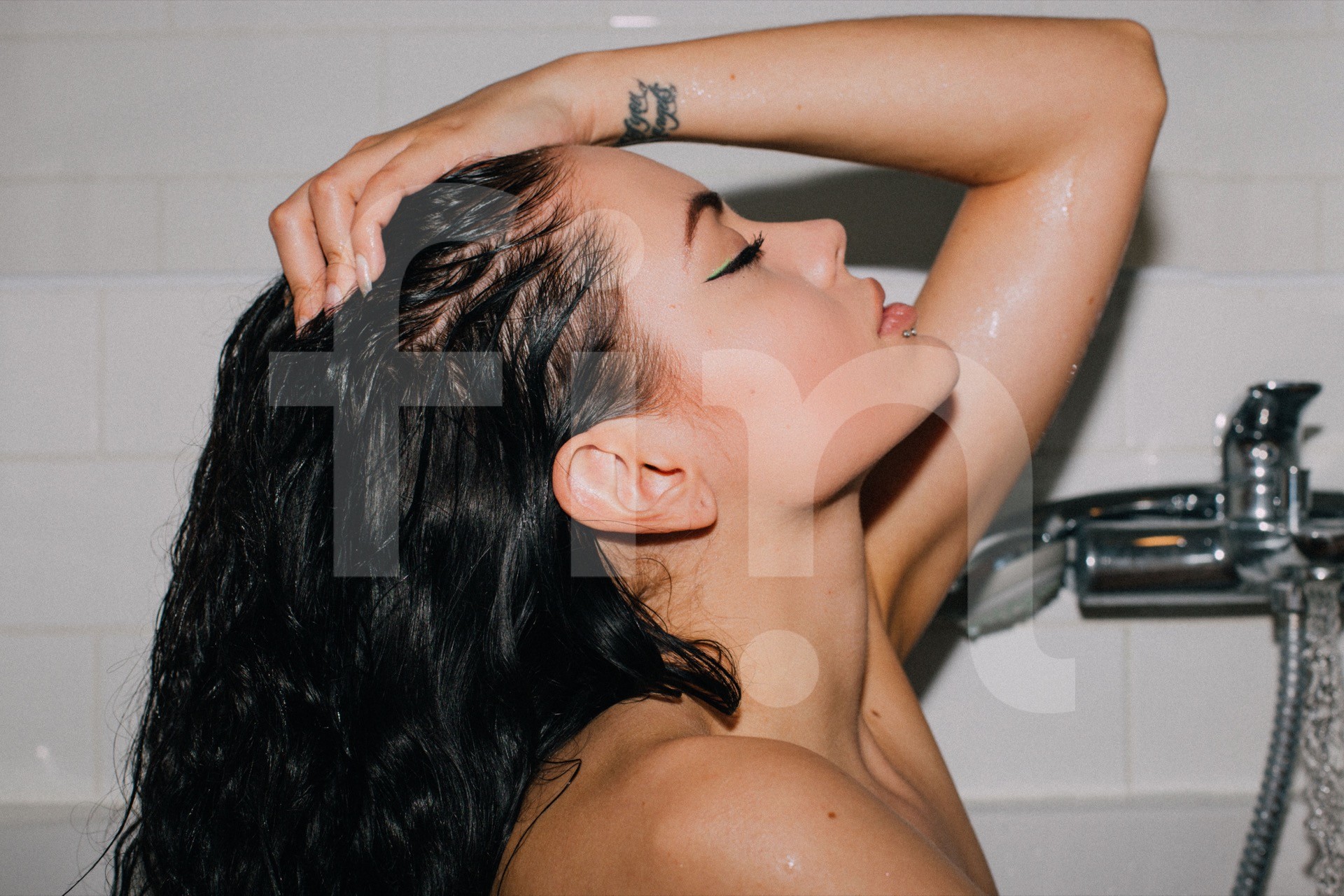 Young girl showers in a bathtub as she runs her hand through her hair with her eyes closed