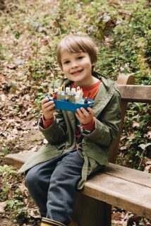 Little kid sitting on bench in nature holding toy ship